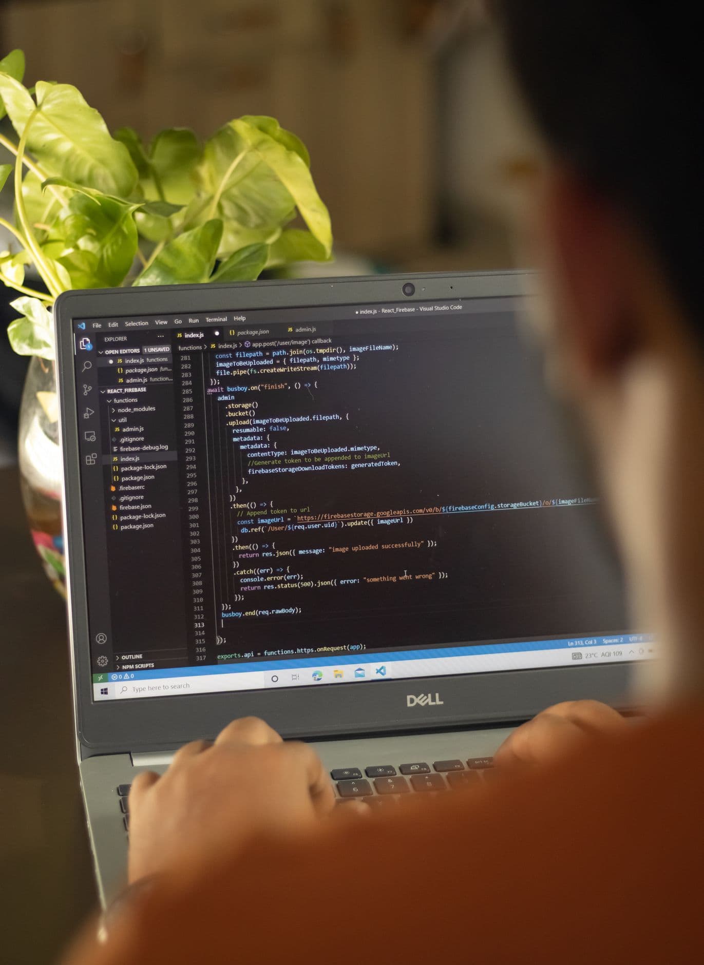 Over the shoulder view of a person writing code in a code editor on a laptop, with a potted plant behind the screen