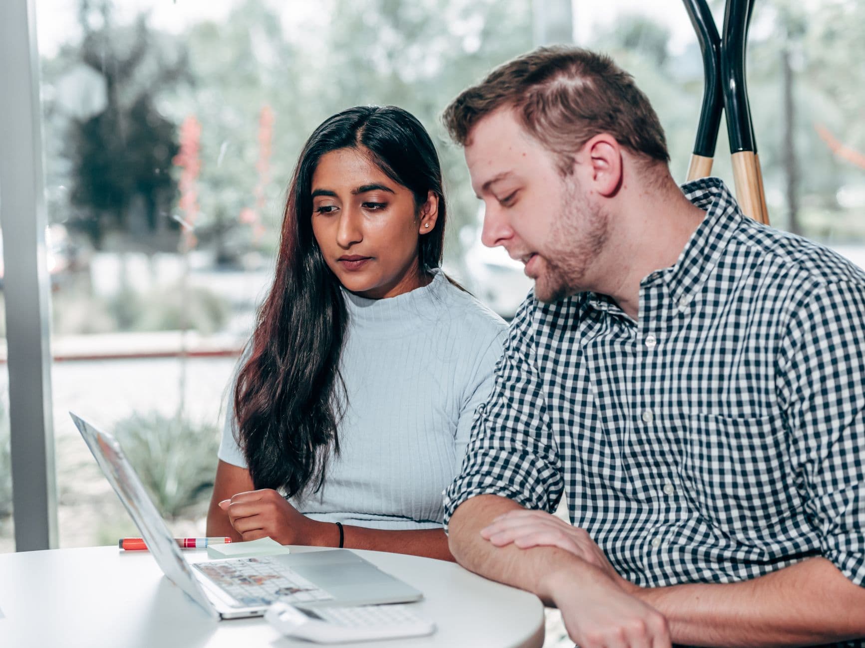Two colleagues sitting side by side and going through work on a laptop at a small round table